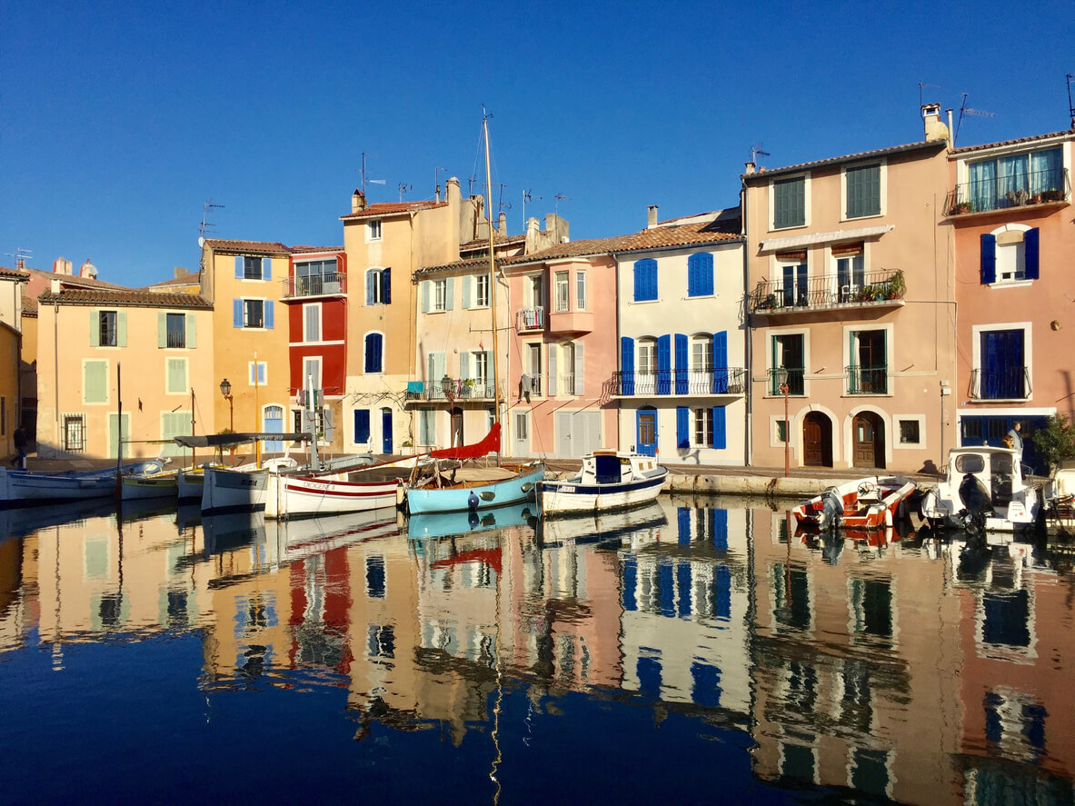 Idyllic photo of a small port of Martigues near Marseille in the "Bouches du Rhône" called bird mirror with colored houses and small boats reflecting on the surface of the water on a sunny day.